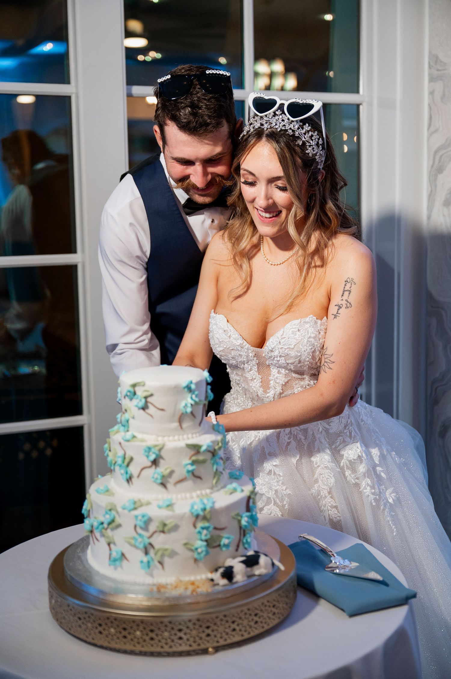 A couple shares a joyful moment while cutting their white and turquoise wedding cake.