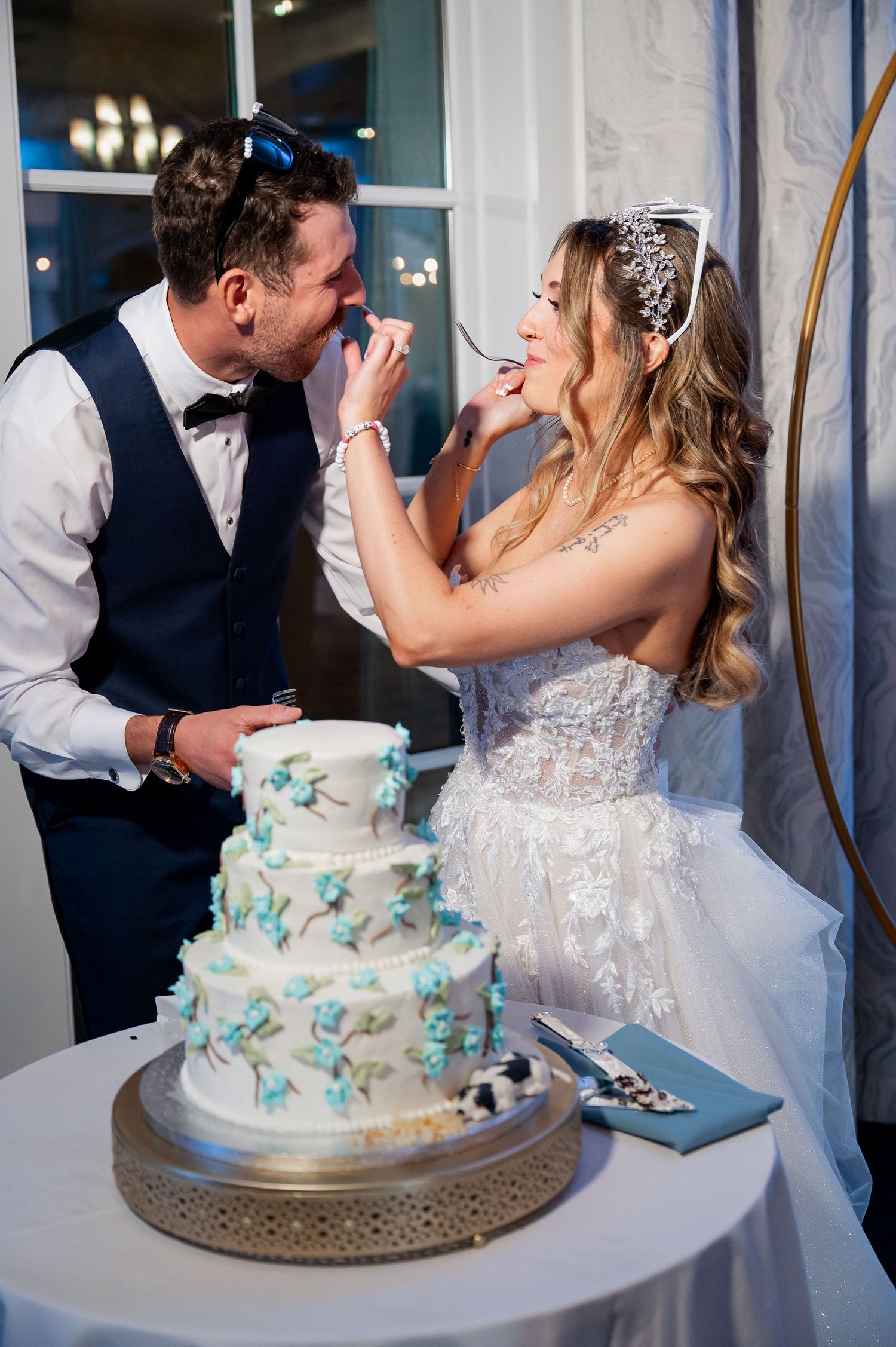 Newlyweds laugh together while preparing to cut their three-tiered white and turquoise wedding cake.