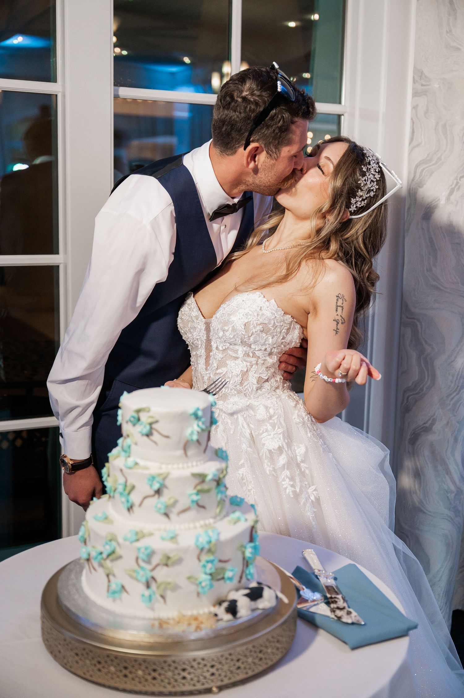 A couple shares their cake cutting moment beside an elegant white and turquoise tiered wedding cake.
