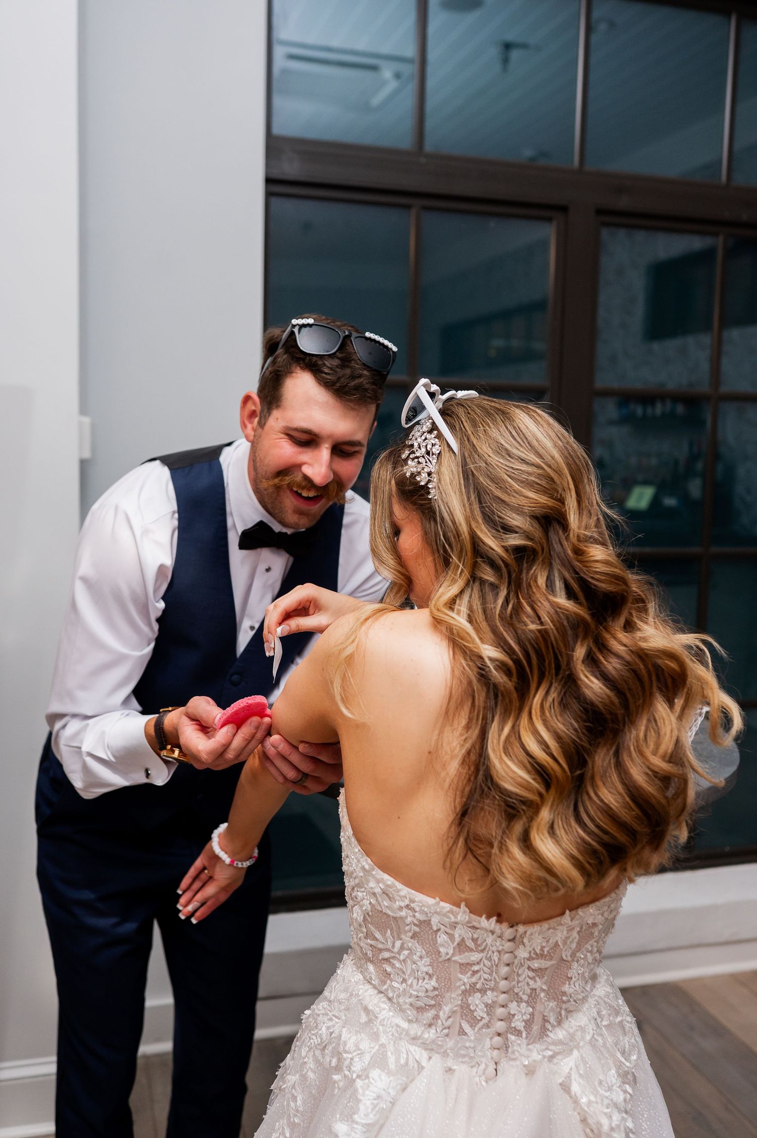 Bride in lace gown and groom in navy vest sharing a fun moment during their reception.