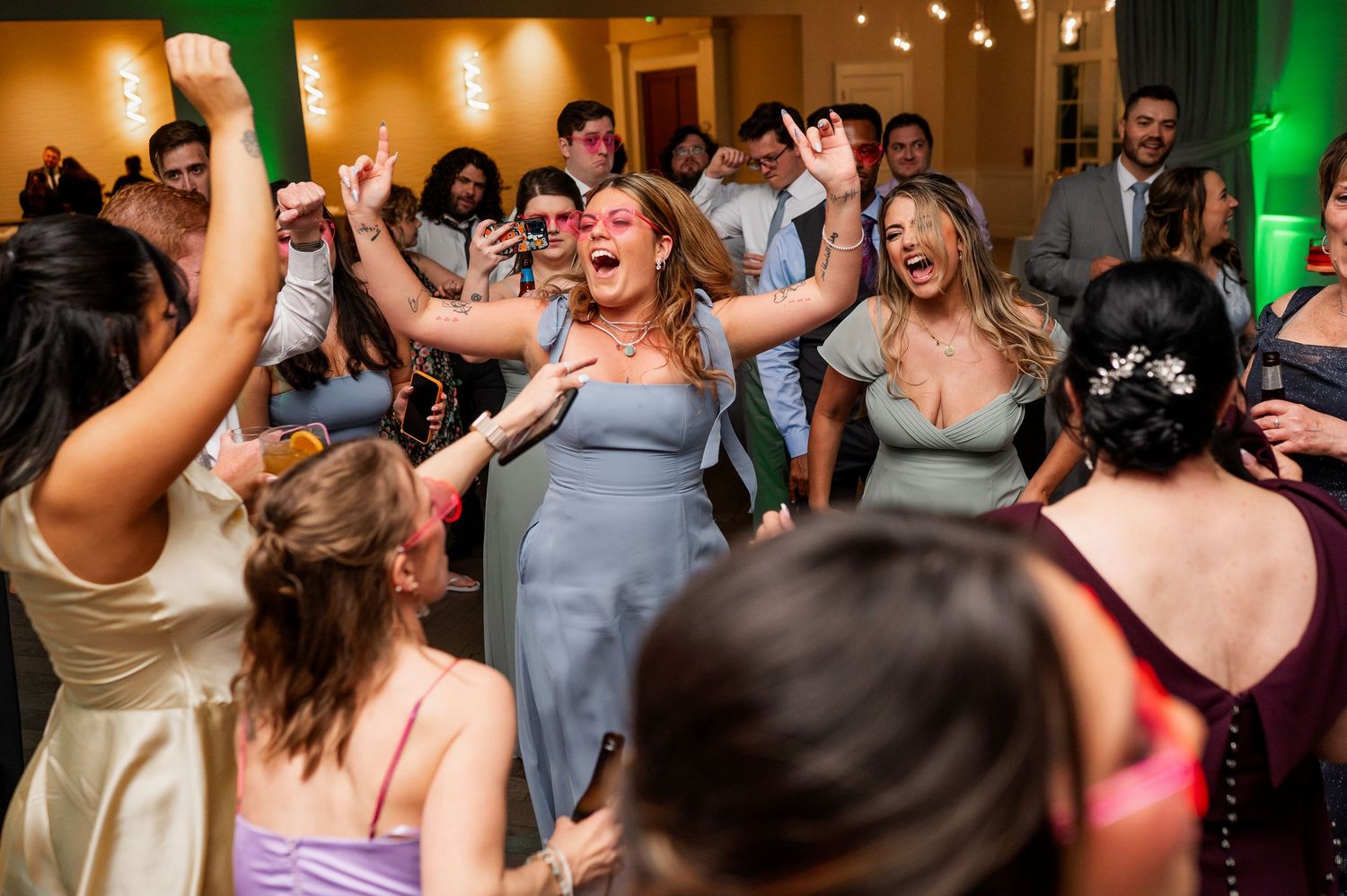 Wedding guests dancing and celebrating under warm lighting at reception venue.