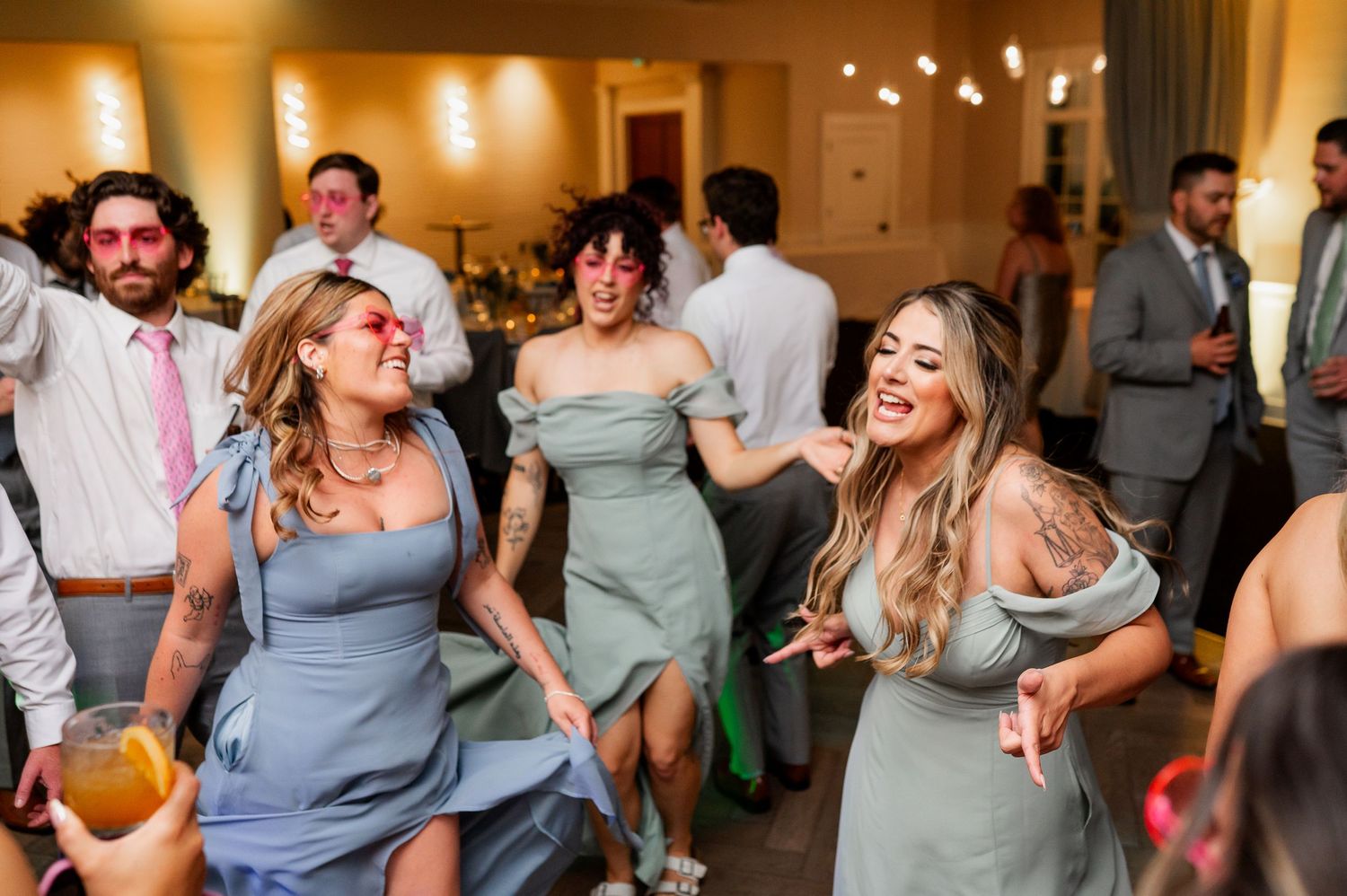 Wedding party and guests dancing energetically at reception with colorful lighting.