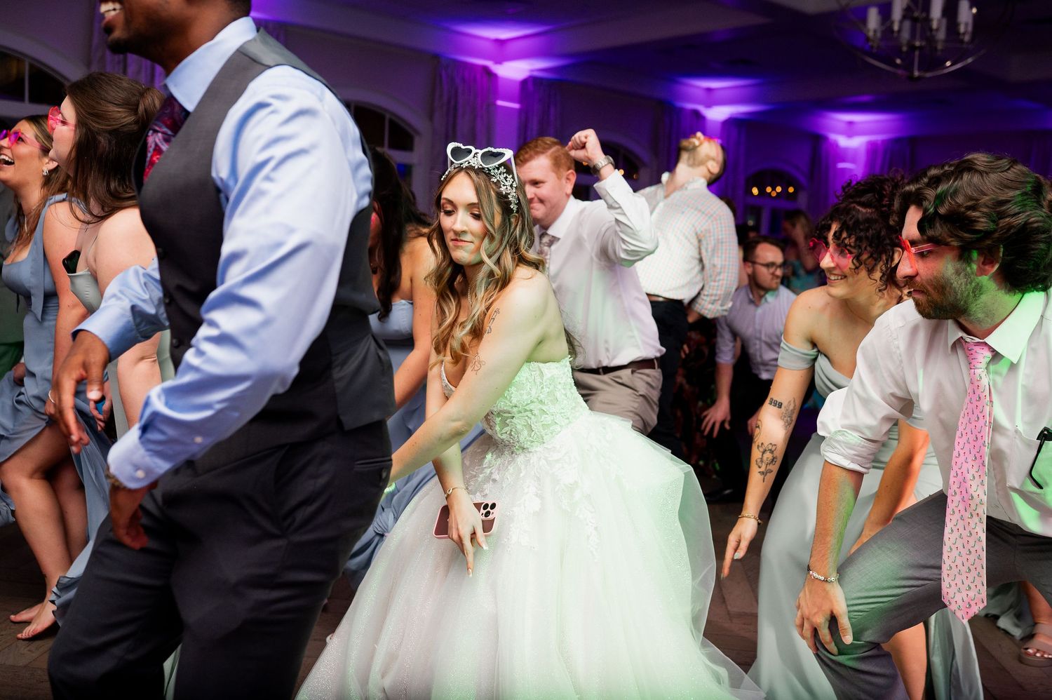 Wedding reception dance floor filled with guests celebrating under purple lighting.