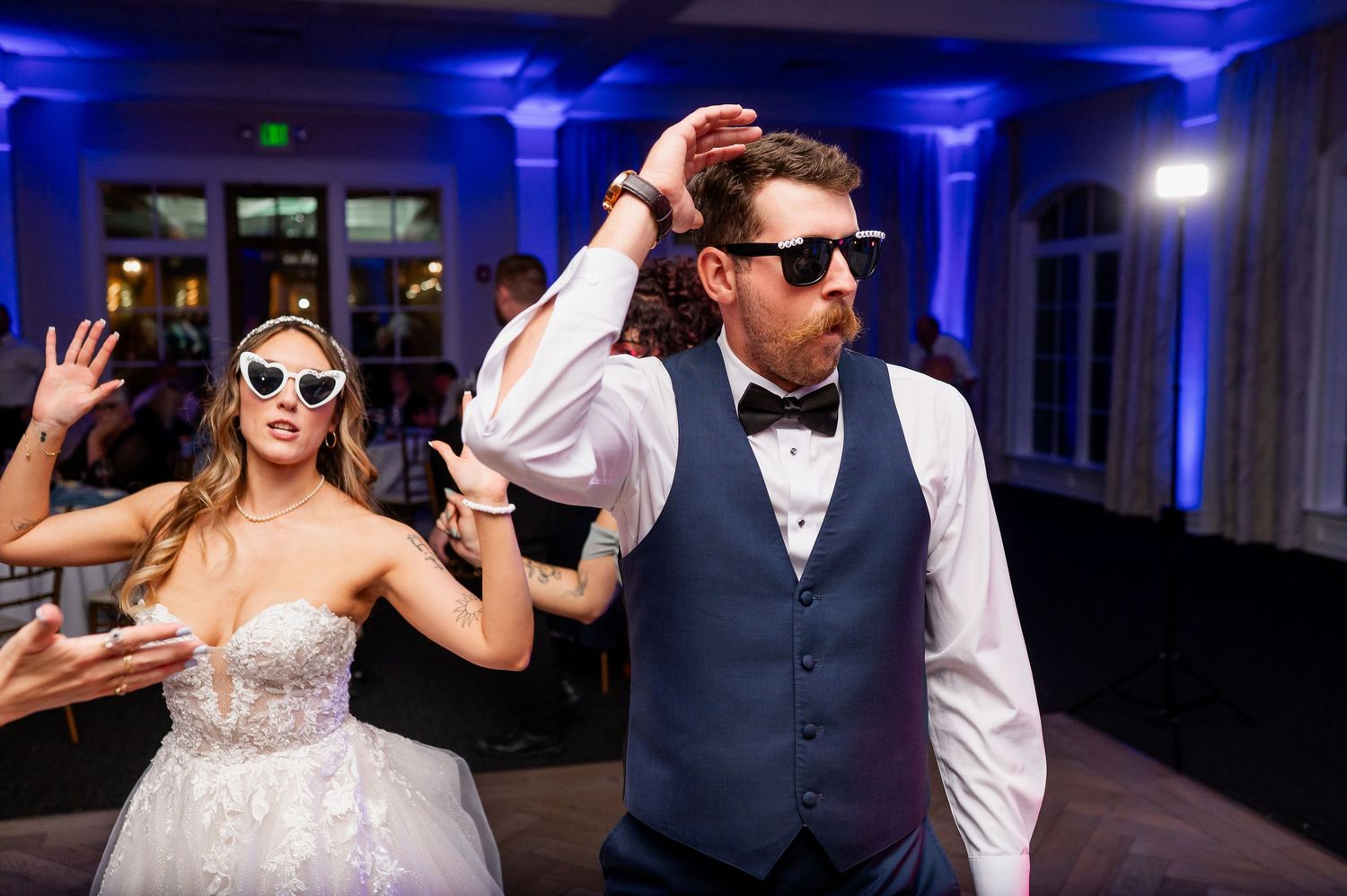 Wedding party dancing under dramatic blue uplighting in an elegant ballroom venue.