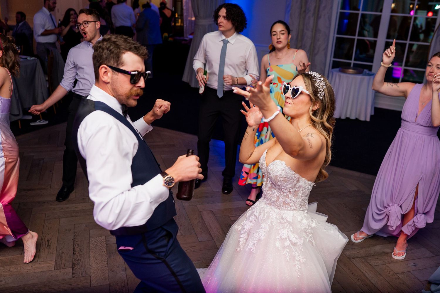 Energetic dance floor moments captured during a wedding reception with purple lighting.