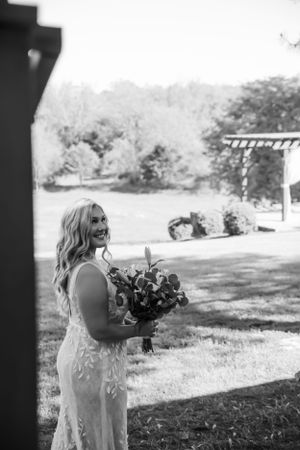 Black and white photo of someone in a lace wedding dress holding a bouquet in a garden setting.
