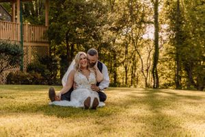 Wedding couple and party take sunset photos on grass near rustic cabin.