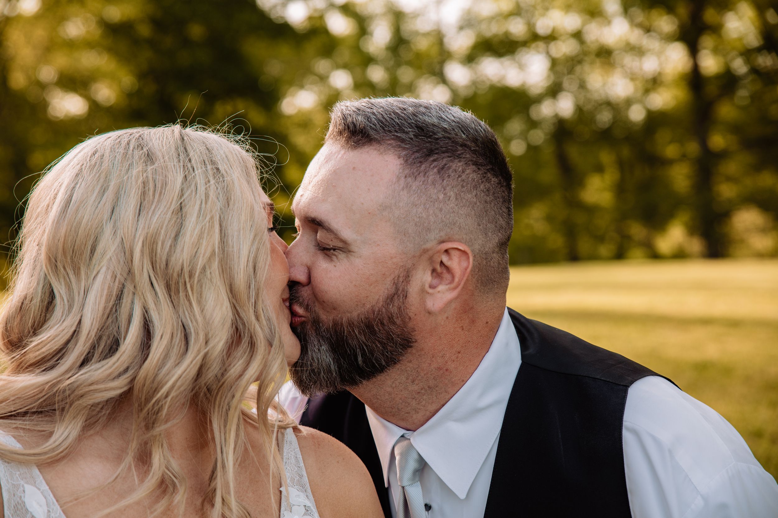 A romantic wedding kiss captured outdoors with golden bokeh lighting in the background.