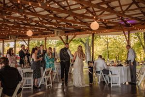 Wedding reception under a rustic wooden pavilion with string lights and paper lanterns creating a warm atmosphere.