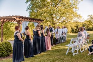 Wedding ceremony setup with white folding chairs and guests in formal attire under autumn trees.