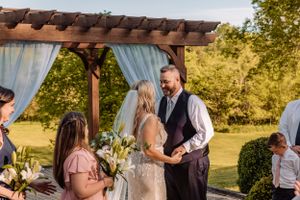 Intimate outdoor wedding ceremony moment under wooden pergola with light blue drapery.