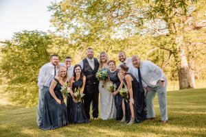 Wedding party members stand together for photos on a grassy hillside at sunset.