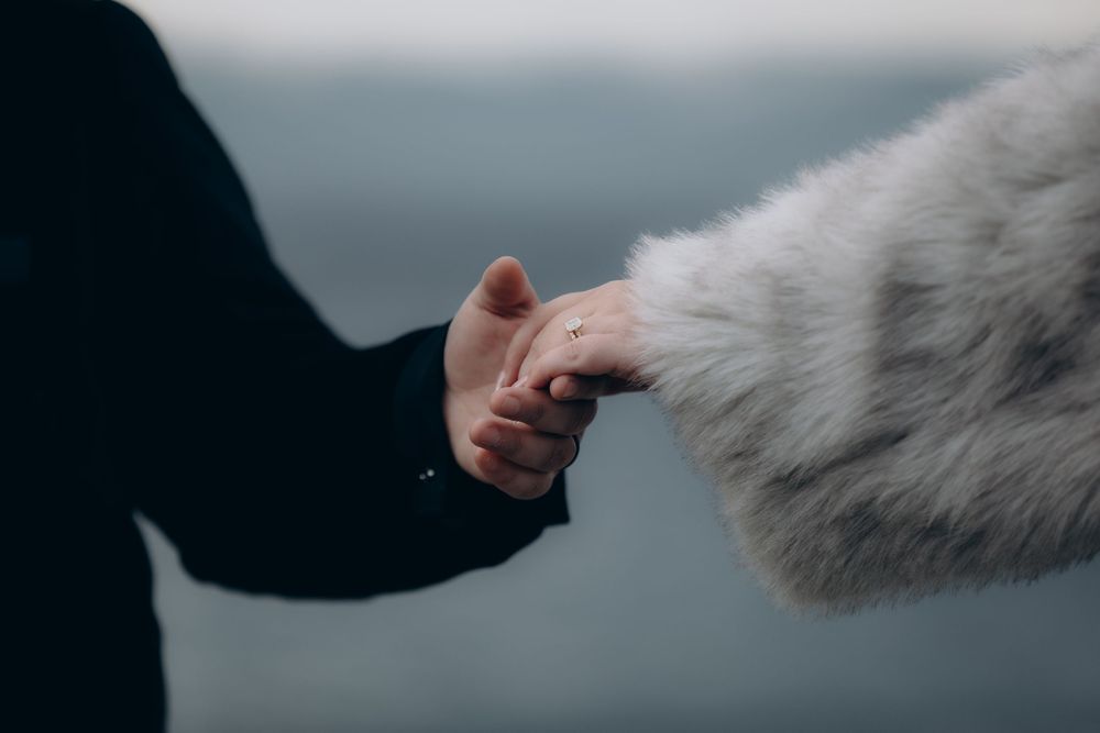 A person's hand gently pets a fluffy white dog's fur against a dark background.