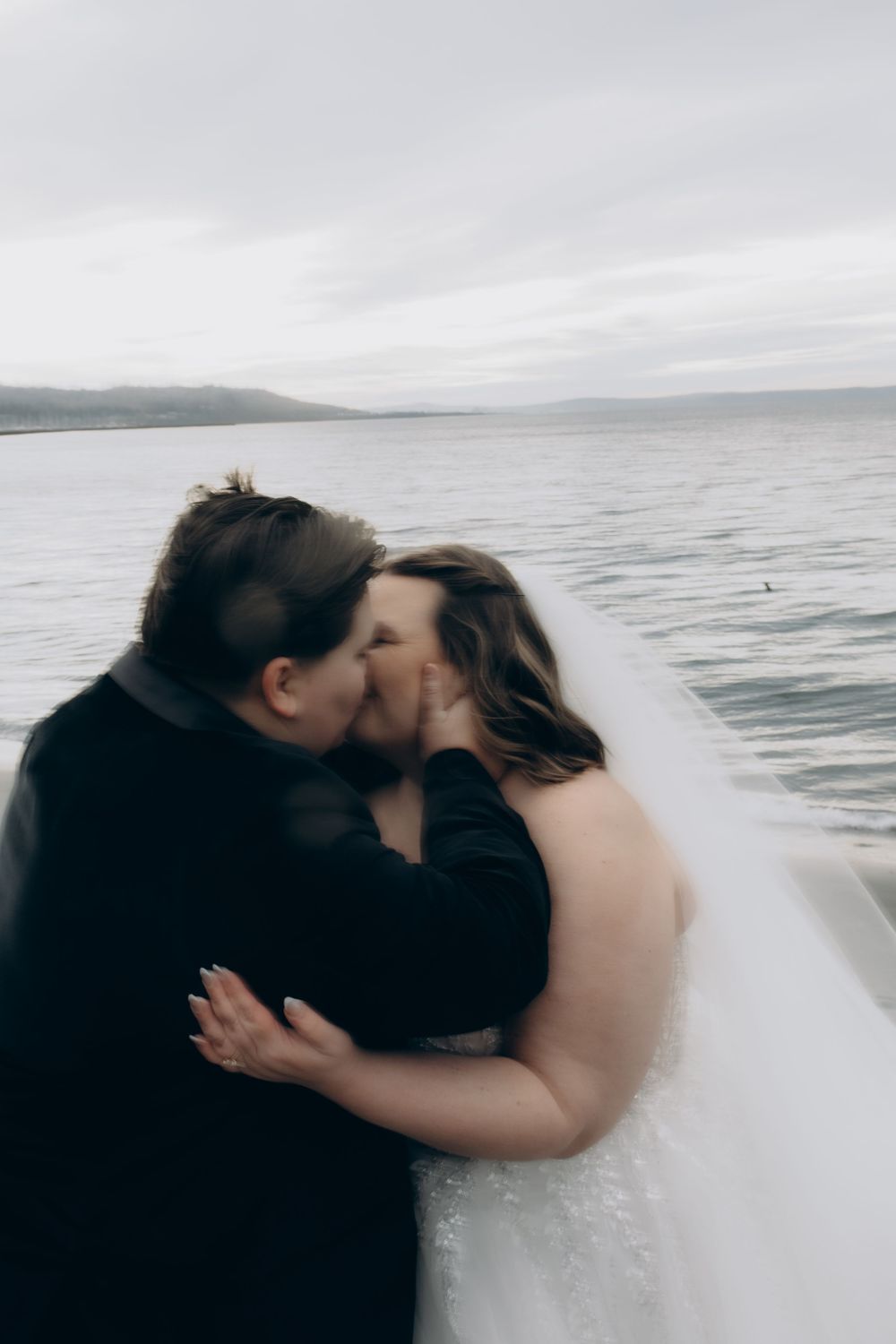 A couple shares a romantic kiss against a misty ocean backdrop on their wedding day.