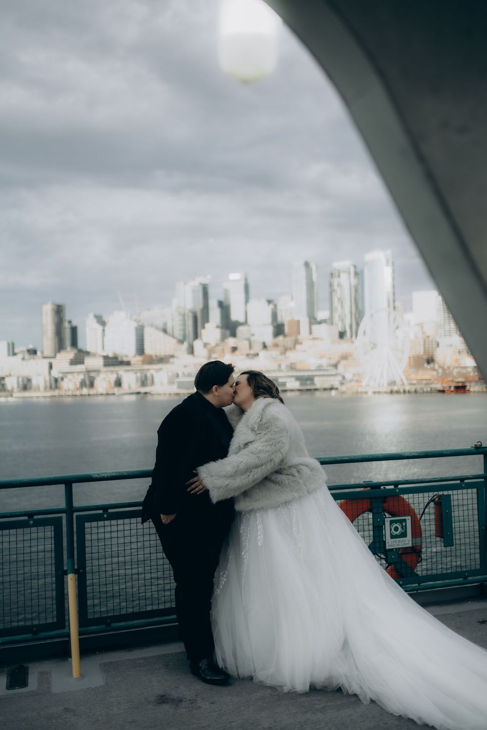 A romantic wedding couple shares intimate moments on a waterfront deck with the Seattle skyline in the background.