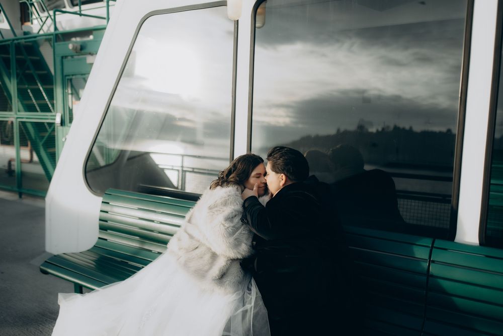 A couple shares a romantic kiss during their wedding photoshoot on a modern glass staircase with dramatic lighting.
