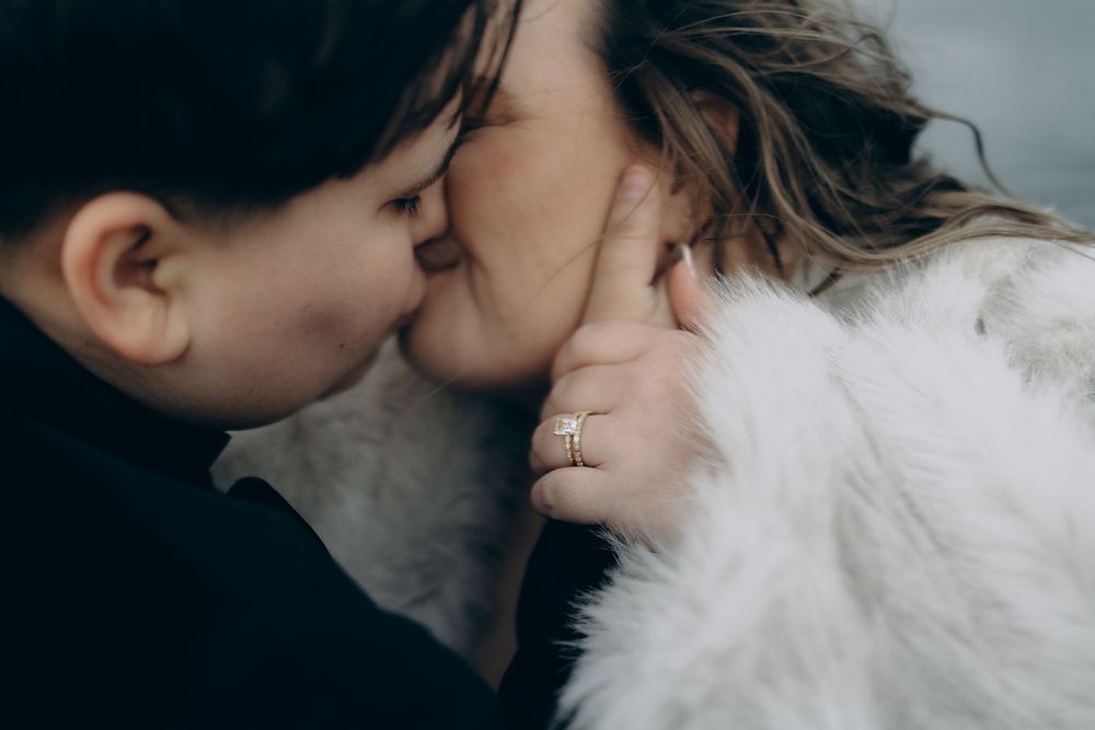A romantic winter engagement photo series showing a couple kissing while wearing cozy white winter attire.