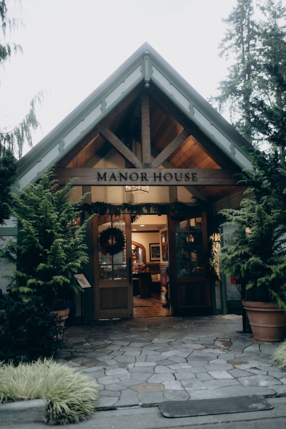 Rustic wooden entrance to Manor House with stone patio and landscaping in Pacific Northwest style.