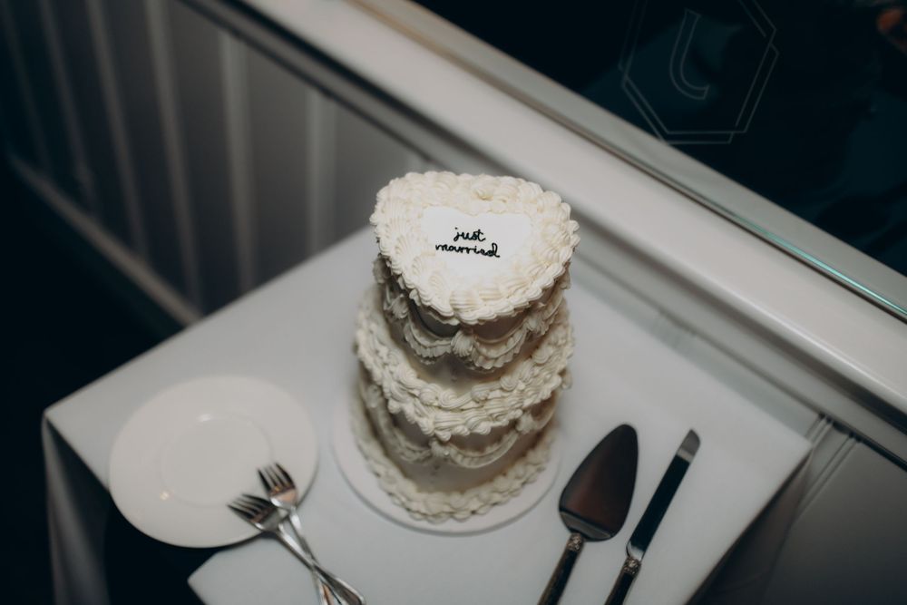 A small white layer cake being frosted with vanilla buttercream on a white plate against a dark background.
