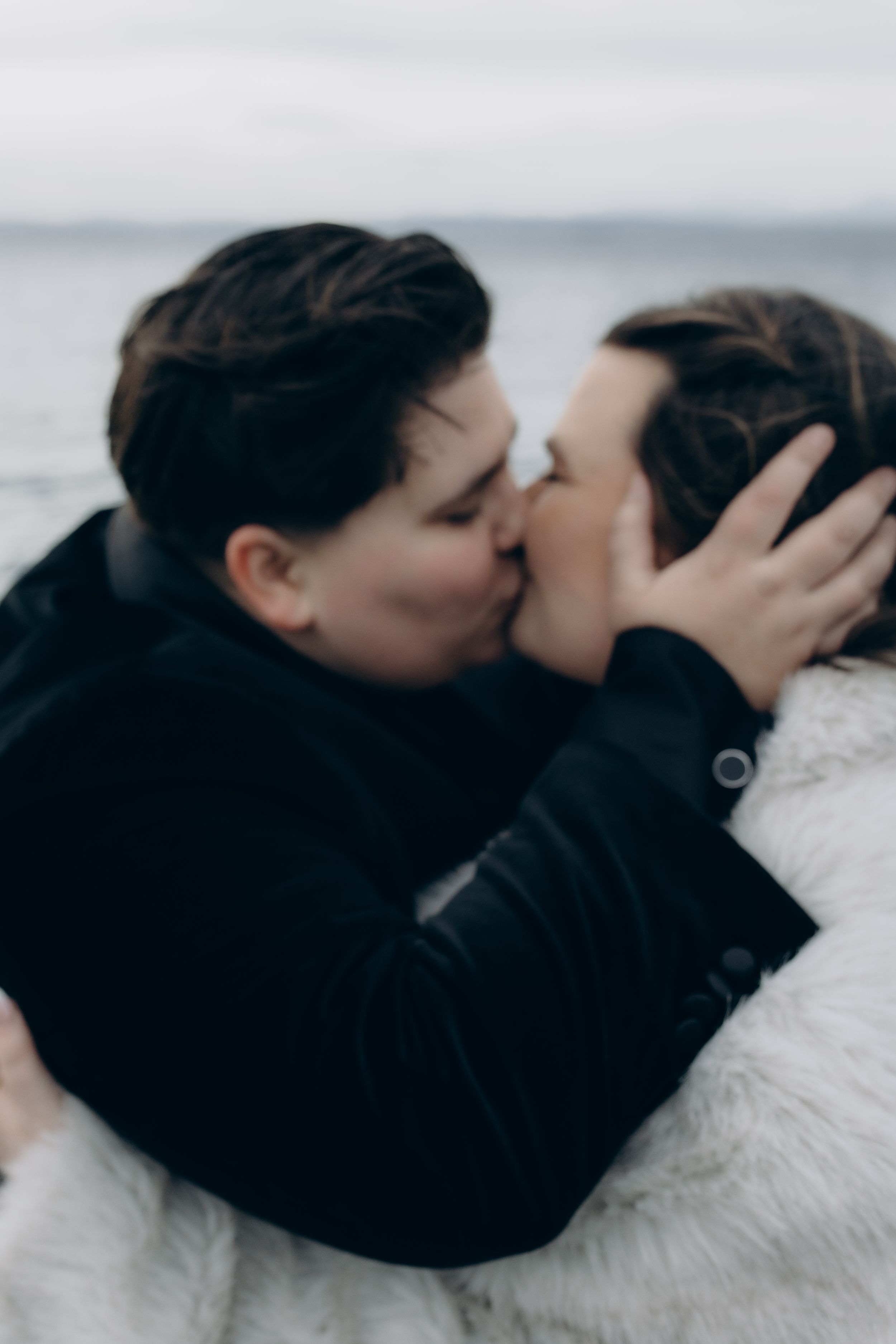 An intimate close-up black and white photo of a couple sharing a tender kiss against a blurred background.