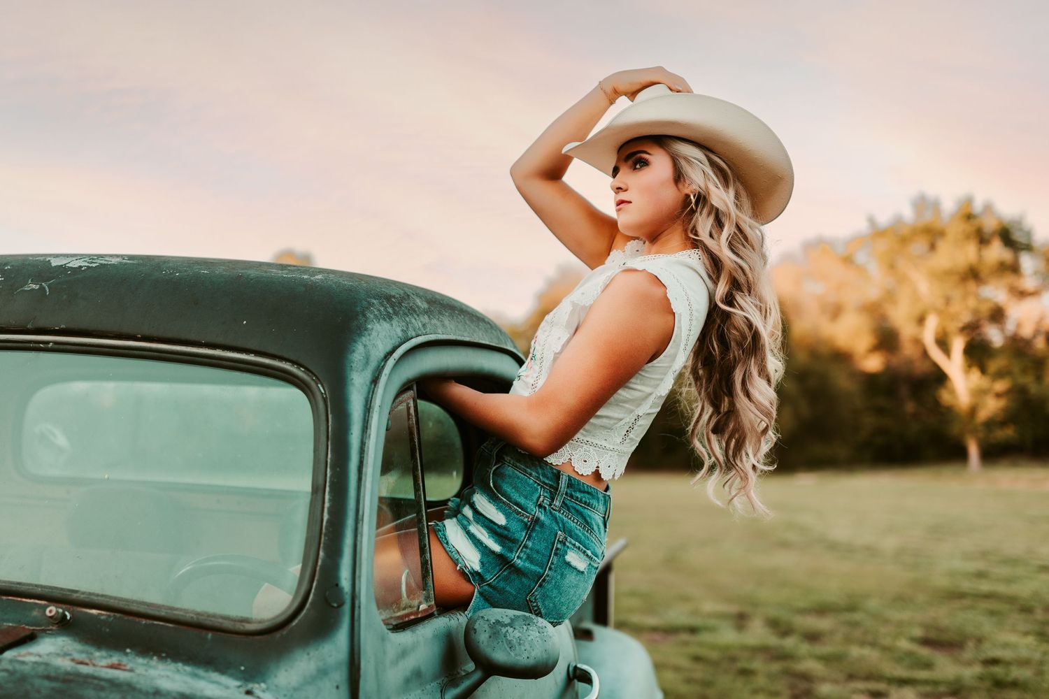 A vintage teal truck parked in a golden sunset field creates a dreamy rustic scene for a summer photoshoot.