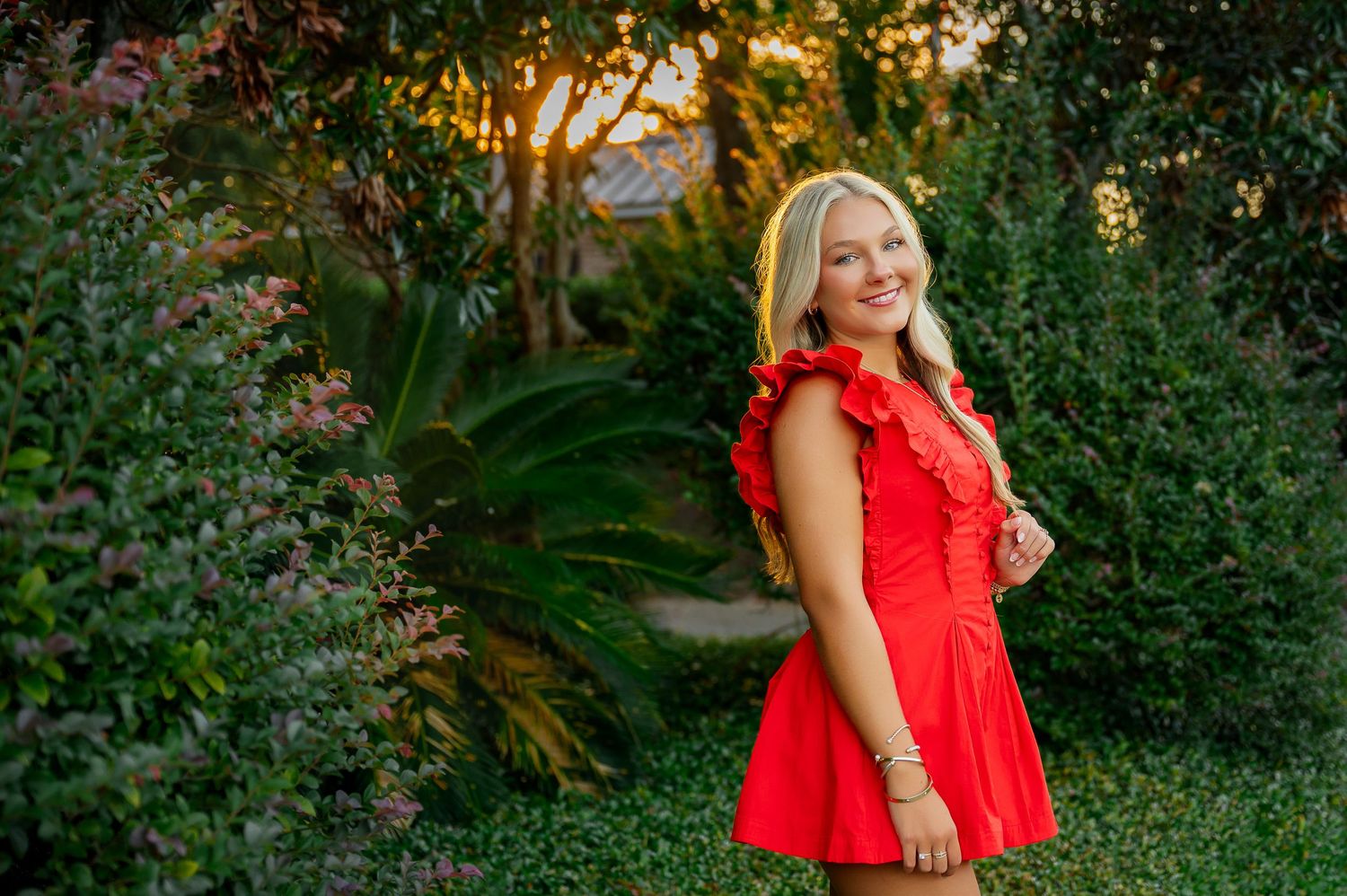 Red sleeveless top against lush green garden background in golden evening light.