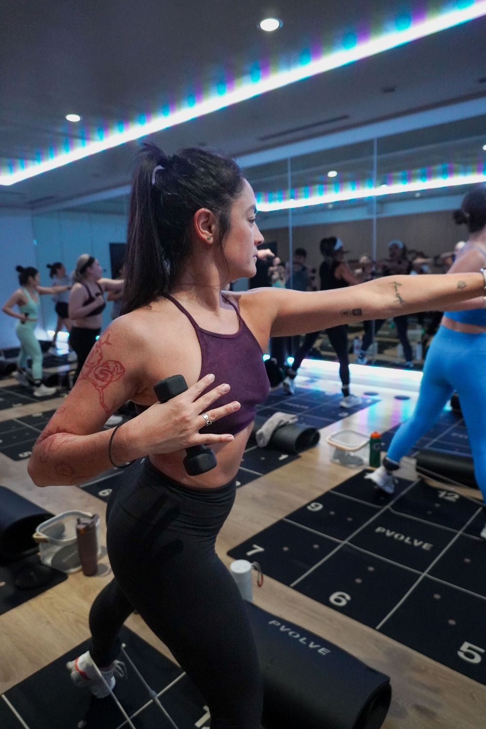 A fitness enthusiast works out in a modern gym studio with colorful LED lighting and mirrored walls.