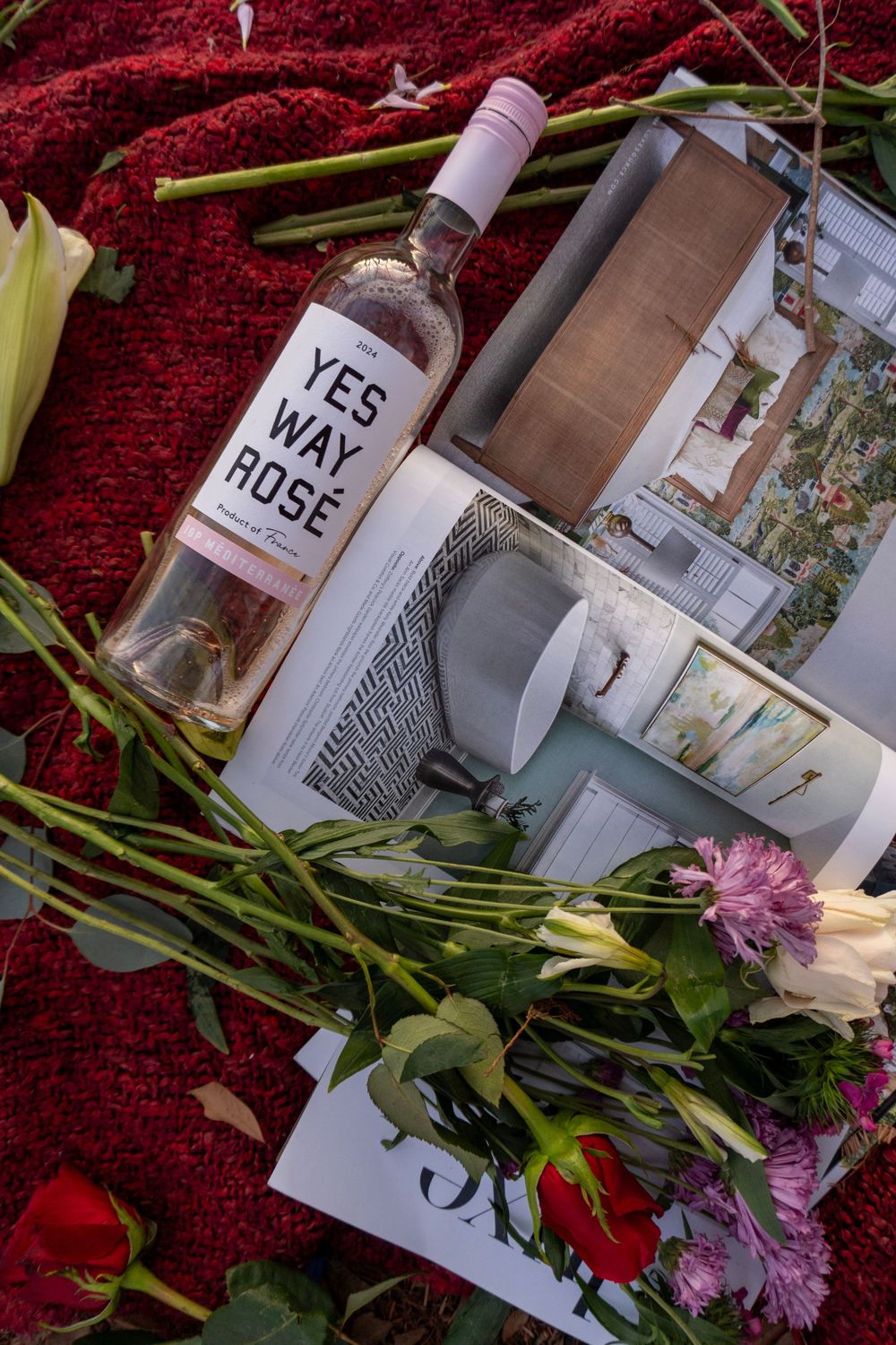 A bottle of Yes Way Rose wine with flowers and photographs arranged on a red velvet background.