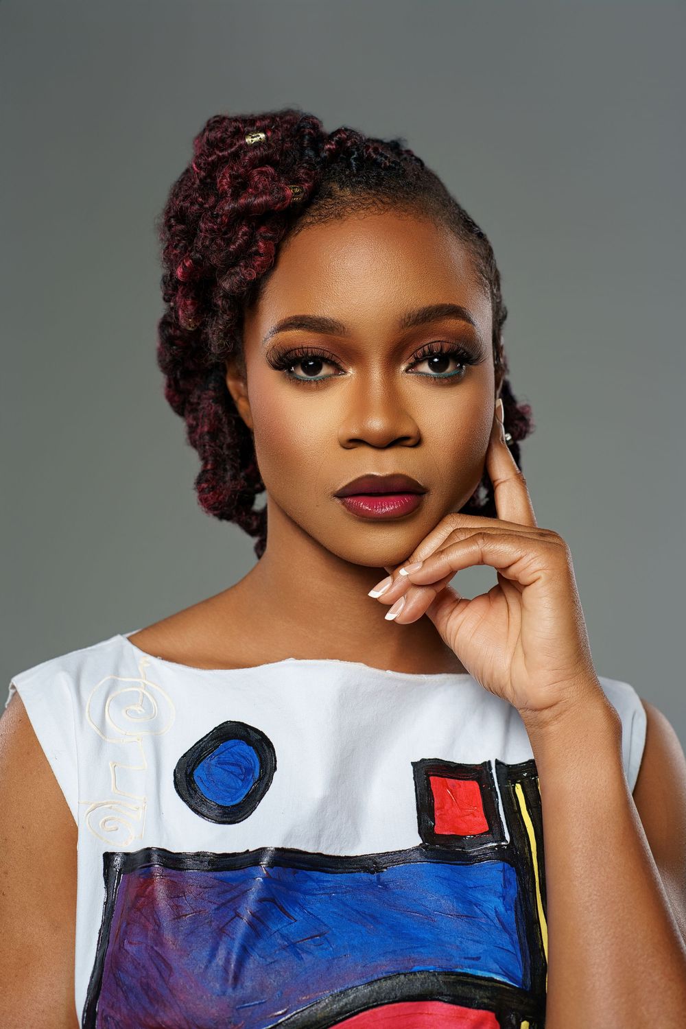 Fashion portrait showcasing a white artistic top with colorful abstract design elements against a gray backdrop.