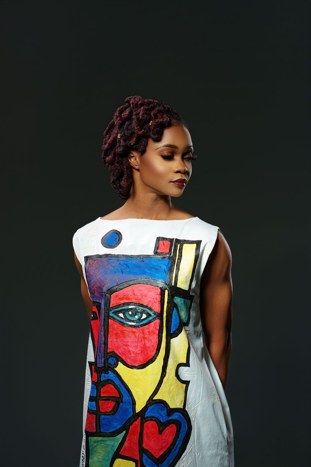 Model wearing a white sleeveless dress with vibrant abstract face art print against dark background.
