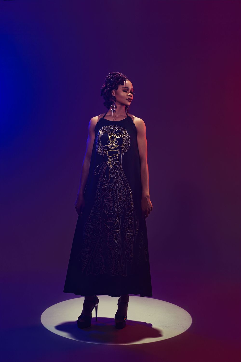 A performer in a sparkly black evening gown stands on an illuminated circular platform against a dark blue backdrop.
