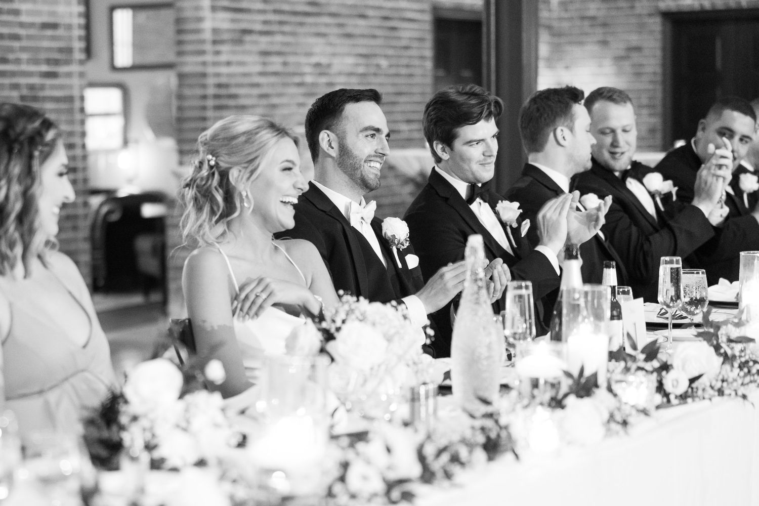 Wedding reception guests dining at long tables in an industrial-style venue with brick walls.