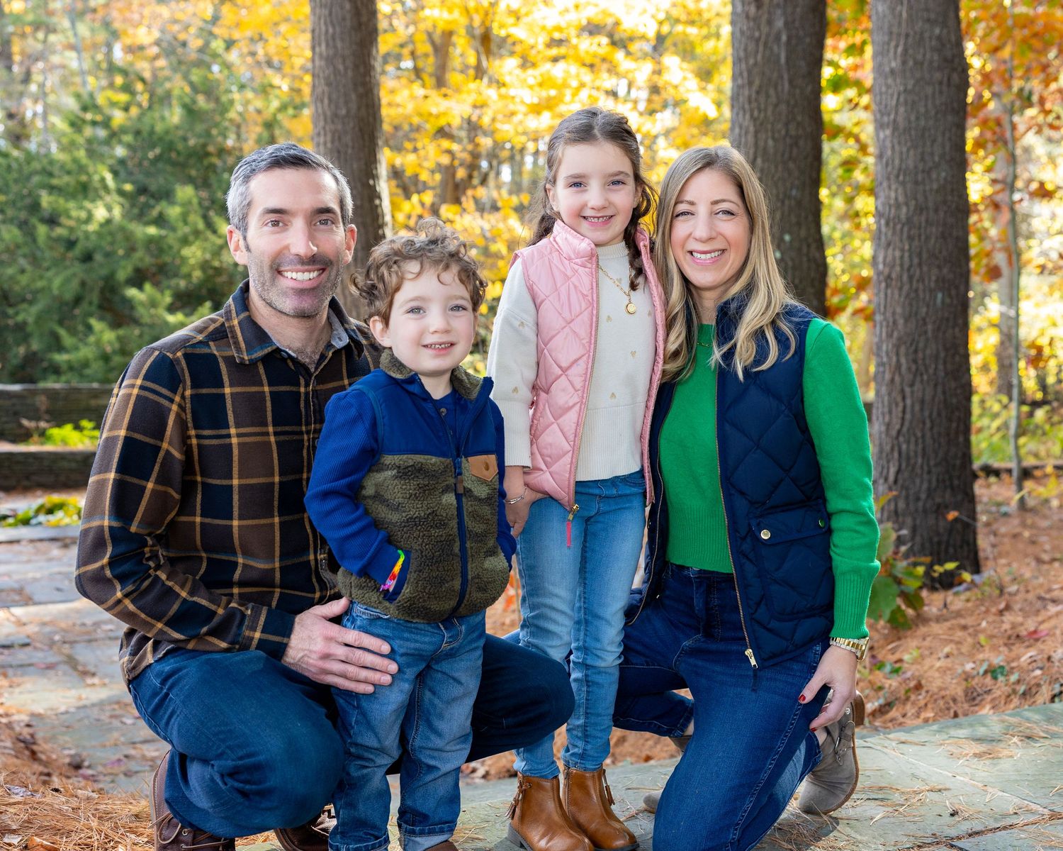 A family poses together outdoors during autumn with colorful fall foliage in the background during family photography session in Sudbury, MA