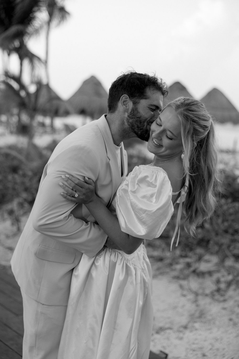 Romantic black and white photo series of a couple sharing intimate kisses on a beach at sunset.