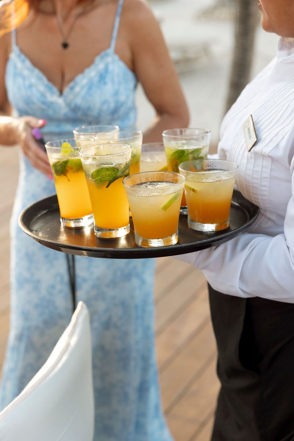 A server carries a tray of refreshing citrus cocktails garnished with mint leaves at an elegant event.