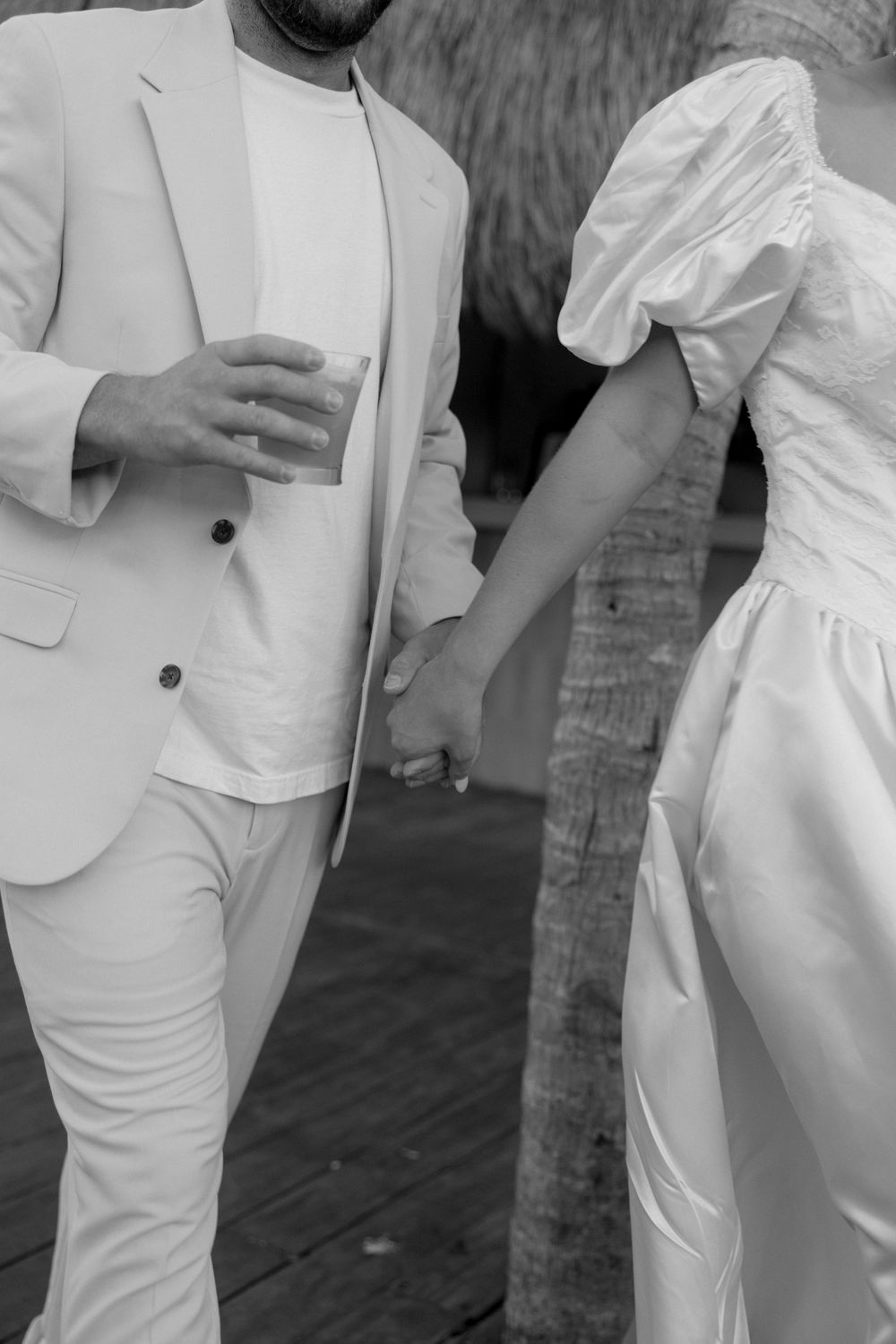 A group wearing elegant all-white outfits stands together at an outdoor event with palm trees in the background.