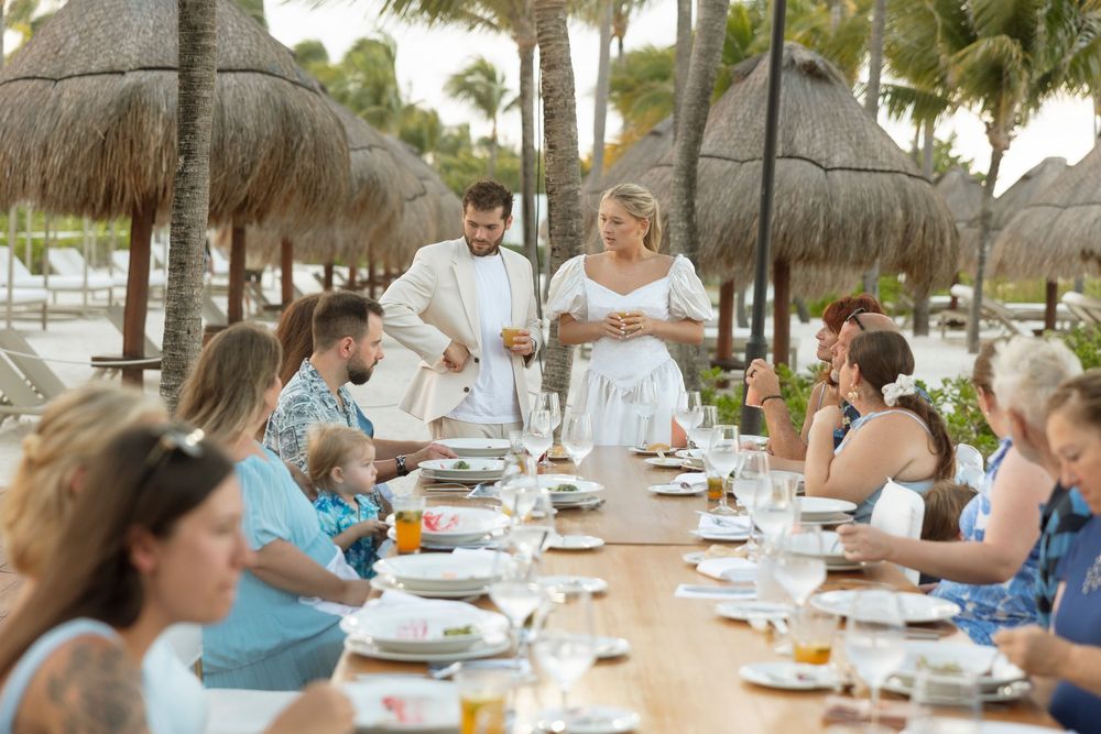 People enjoying a casual outdoor dining experience under thatched roof palapas at a tropical resort restaurant.