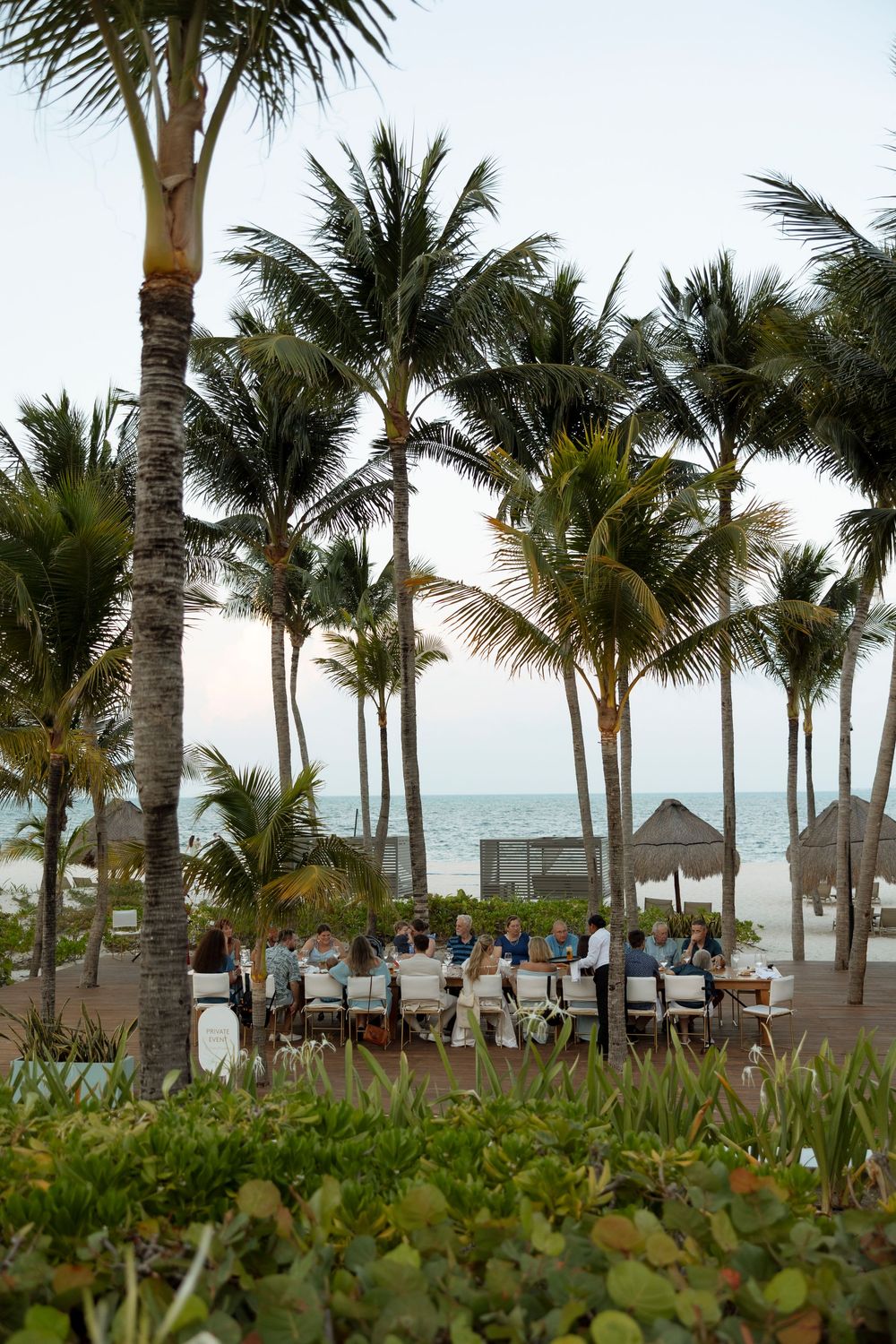 Palm trees line a tropical beach resort boardwalk with thatched umbrellas and ocean views.