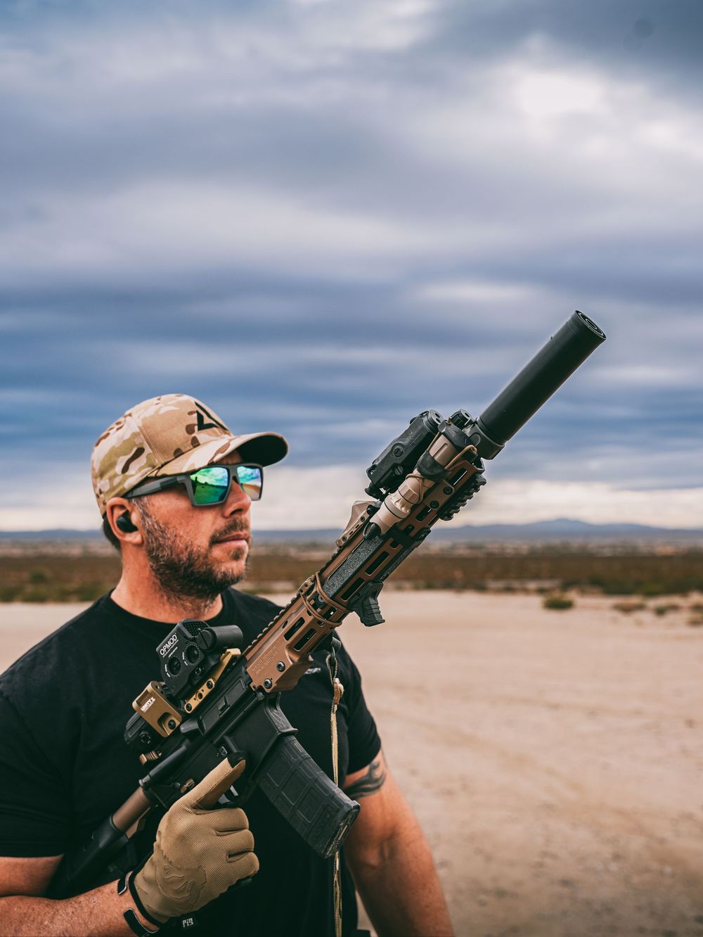 A tactical shooter standing with an AR-style rifle in a desert setting under cloudy skies.