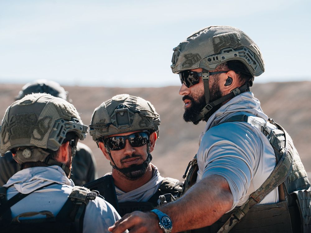 Group of operators in tactical gear coordinating during desert training exercise.