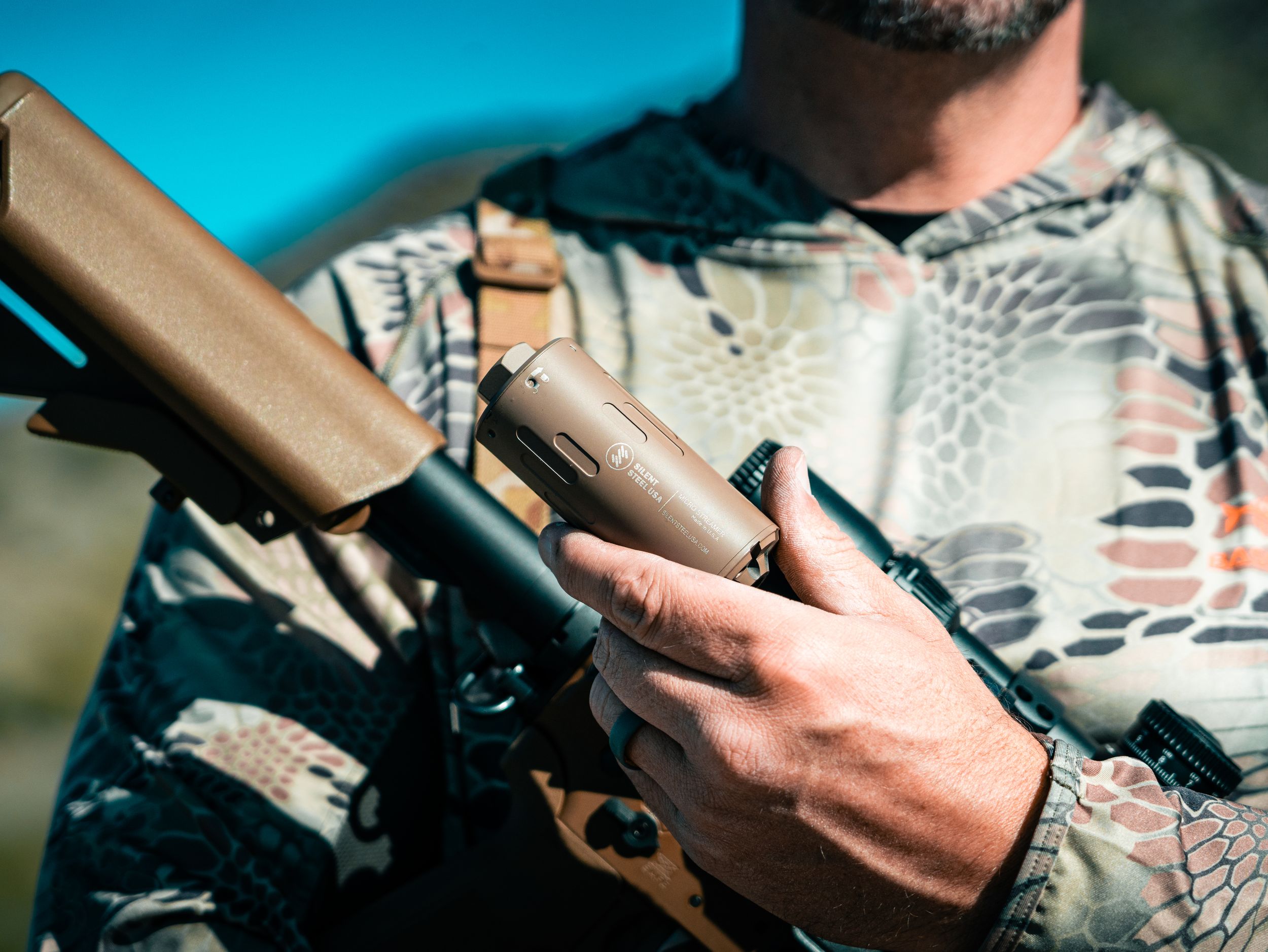 Close-up of hands holding tactical rifle components in desert environment.
