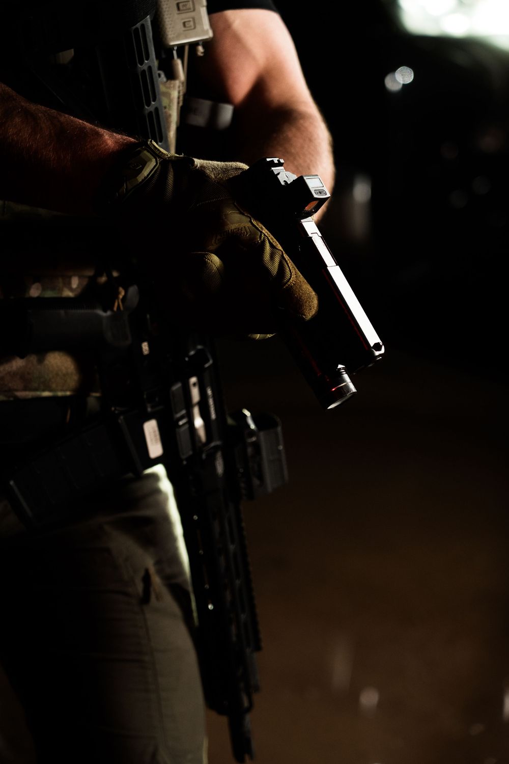 Close-up shot of gloved hands manipulating firearm components in low light.