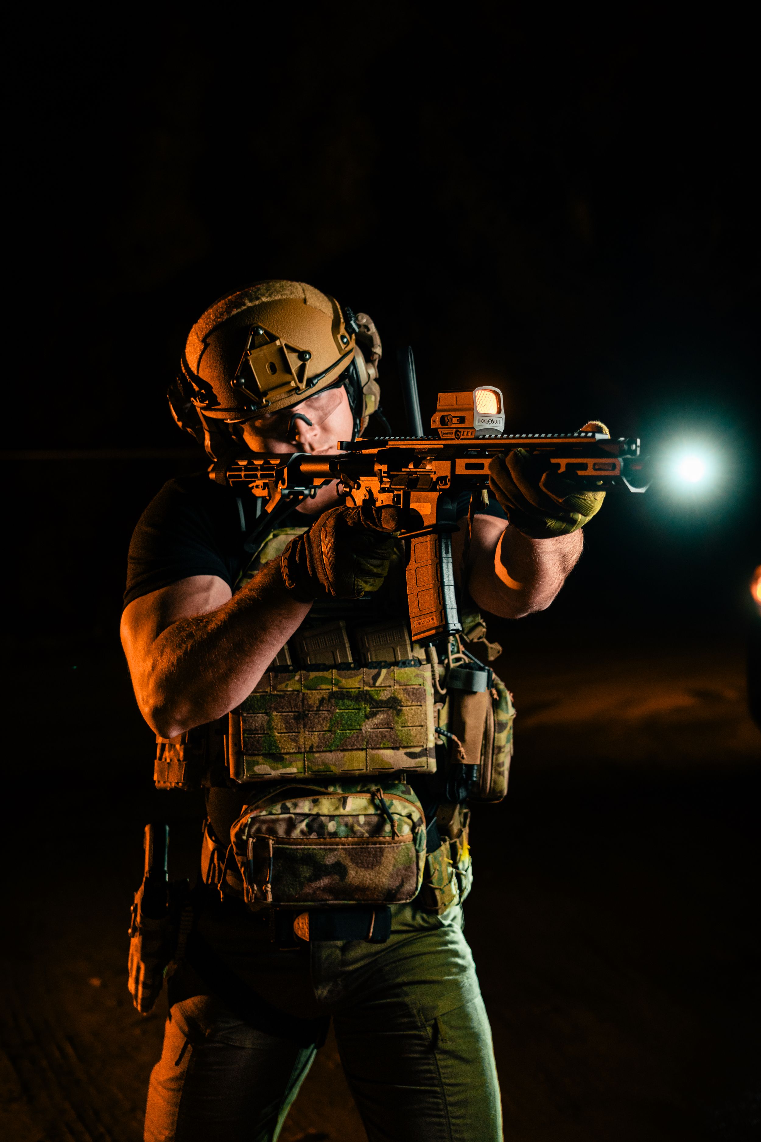Tactical operator in combat gear aiming rifle with mounted light in dark environment.