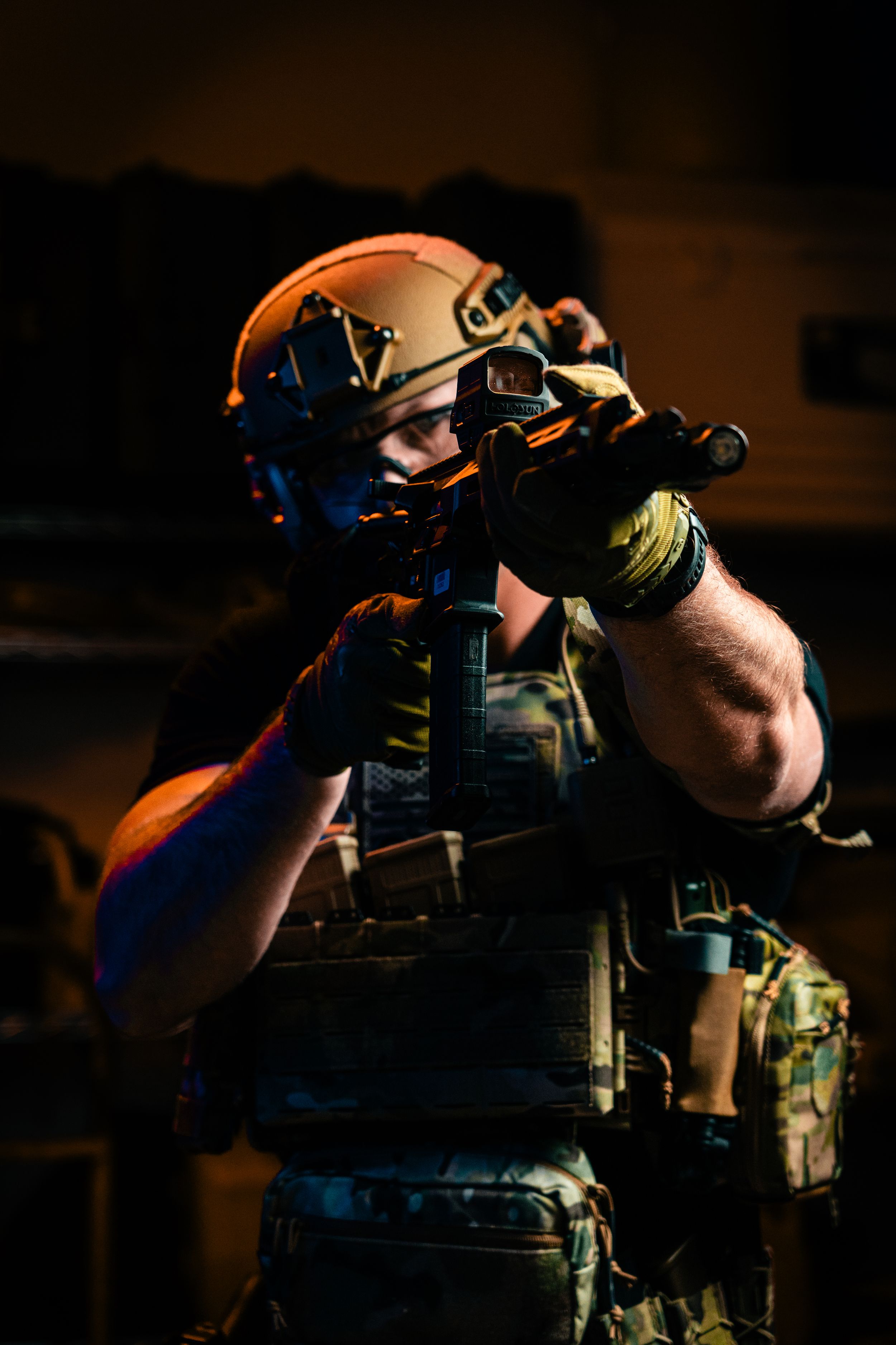 Military operator in tactical gear and helmet aiming with night vision equipment.