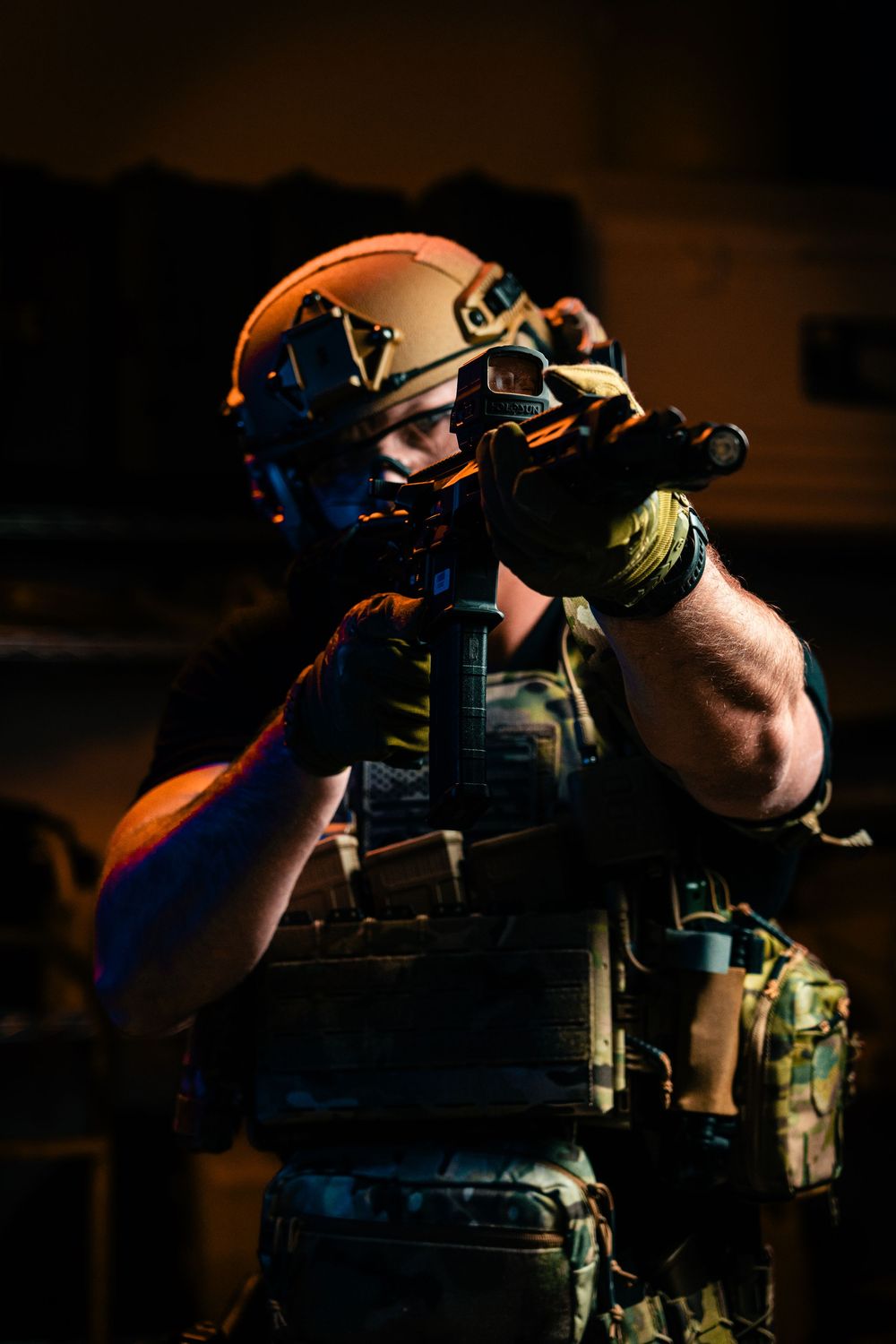 Military operator in tactical gear and helmet aiming with night vision equipment.