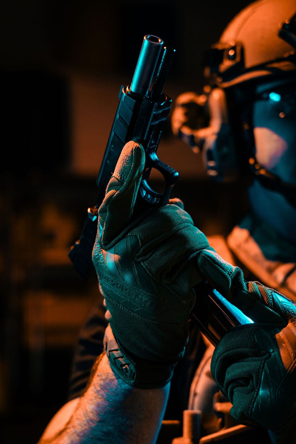 Tactical operator holding a black pistol in low light conditions with orange ambient lighting.
