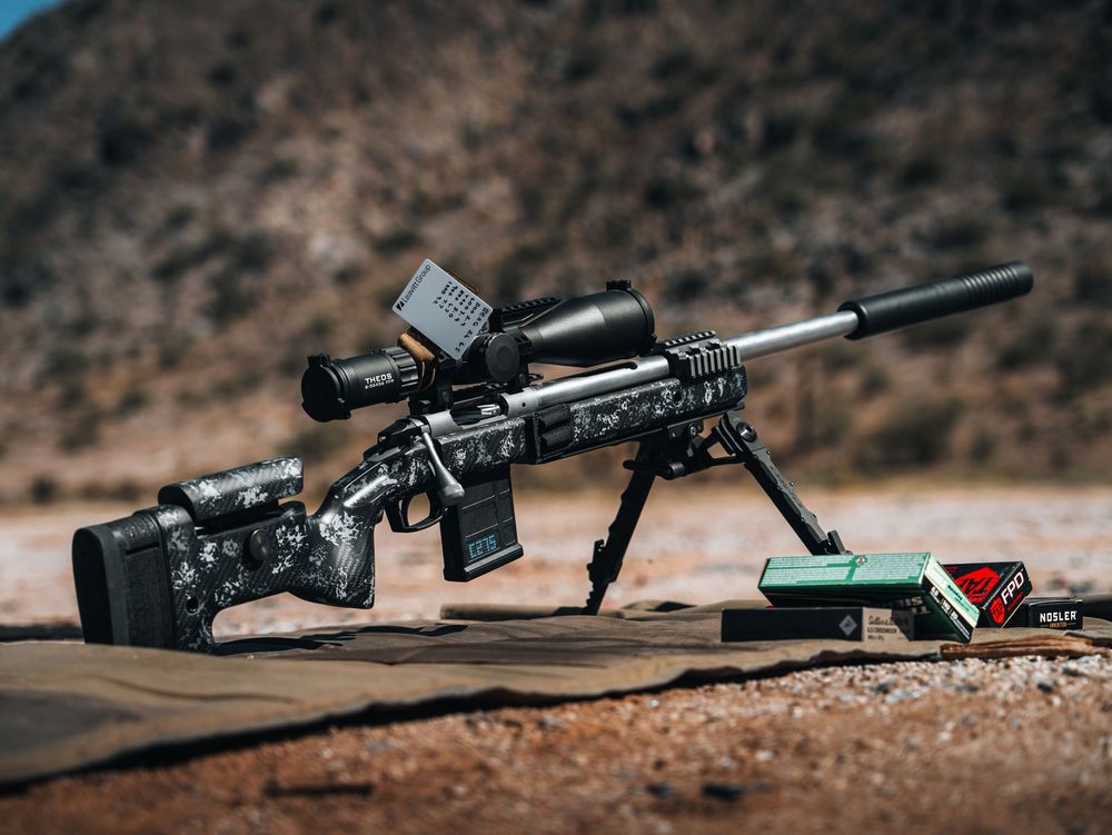 A camouflage-patterned sniper rifle lies on rocky terrain in multiple angles showing its tactical design and features.