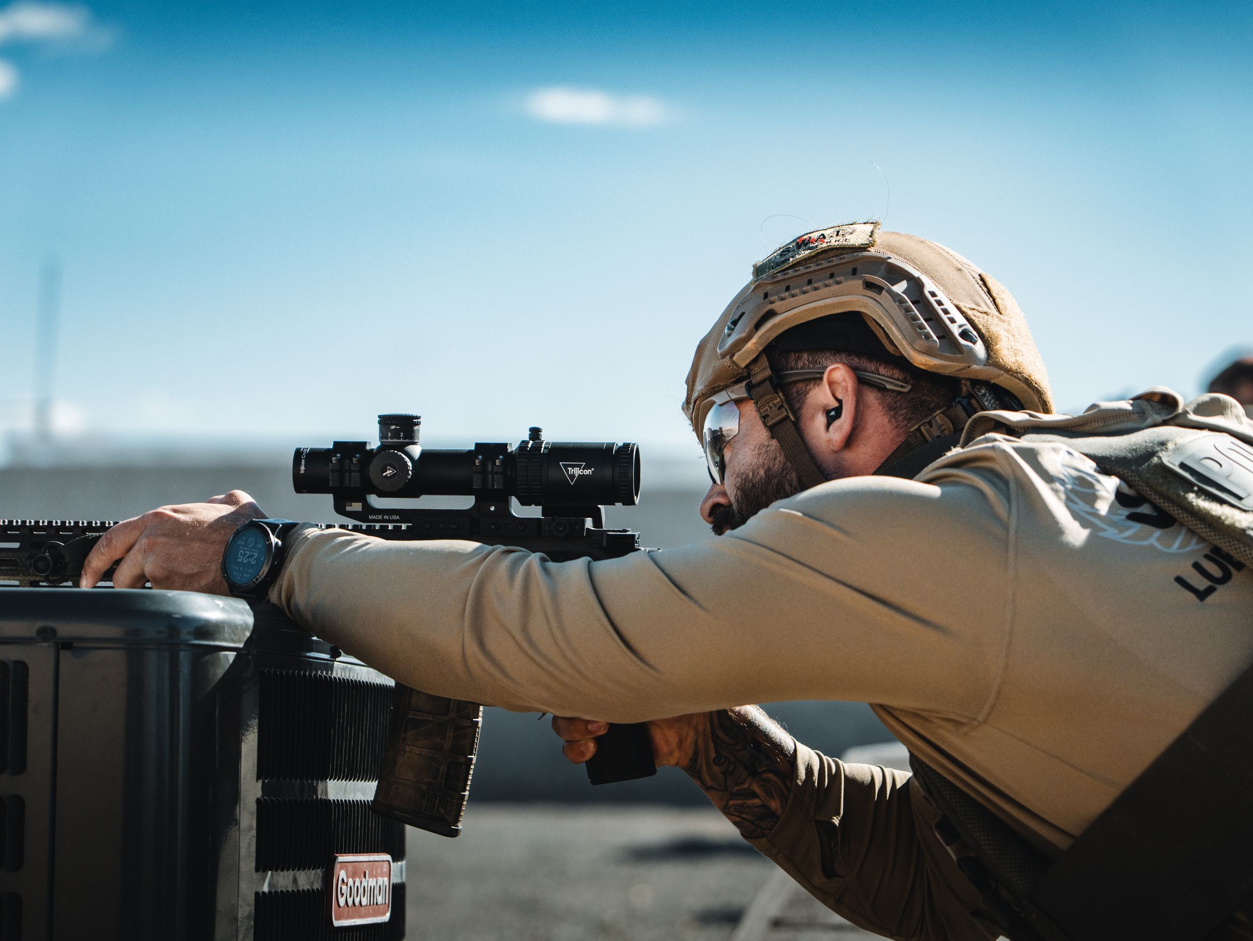 A swat officer taking a shot from behind an ac unit on a roof.