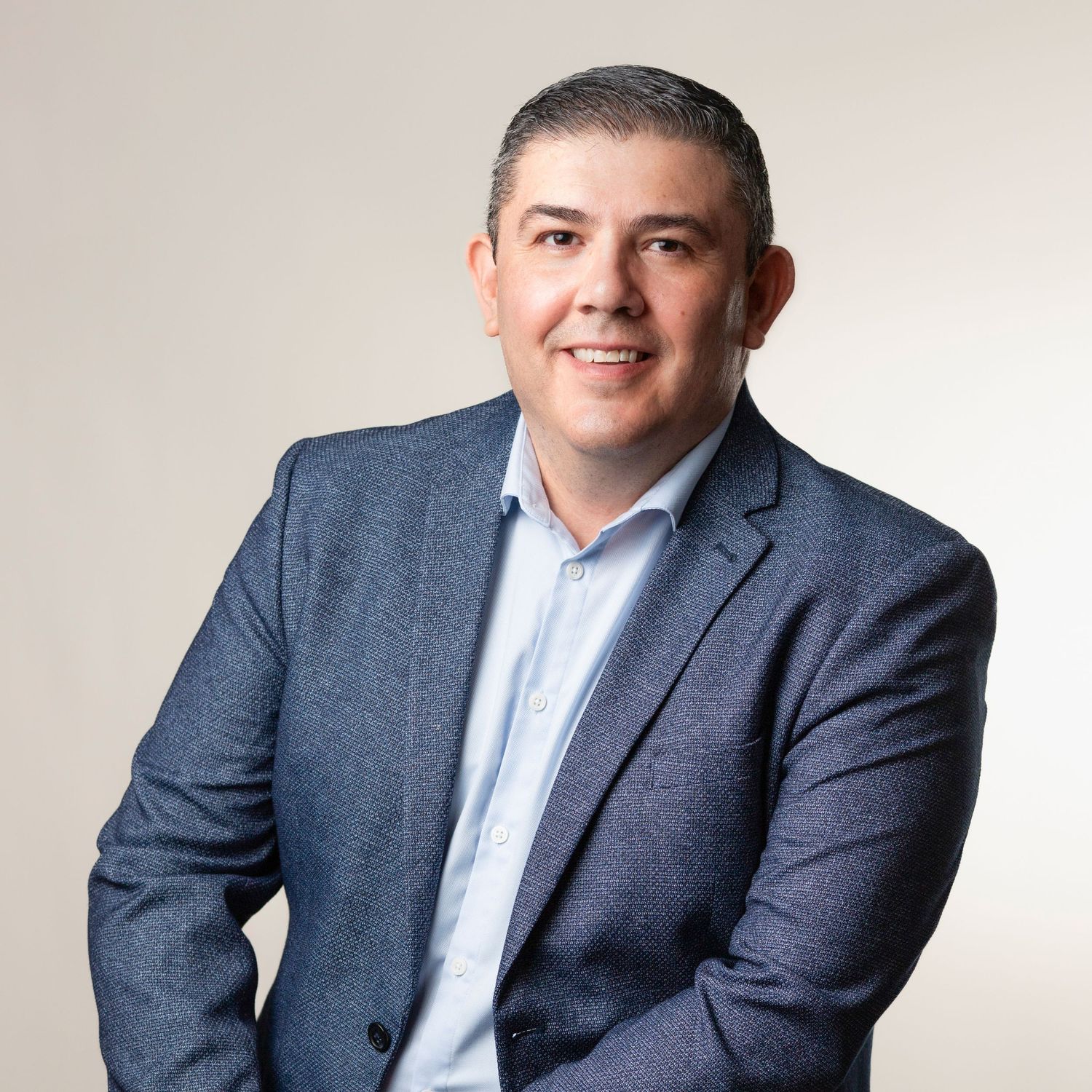Professional headshot of someone in a navy suit and light blue shirt against a neutral background.