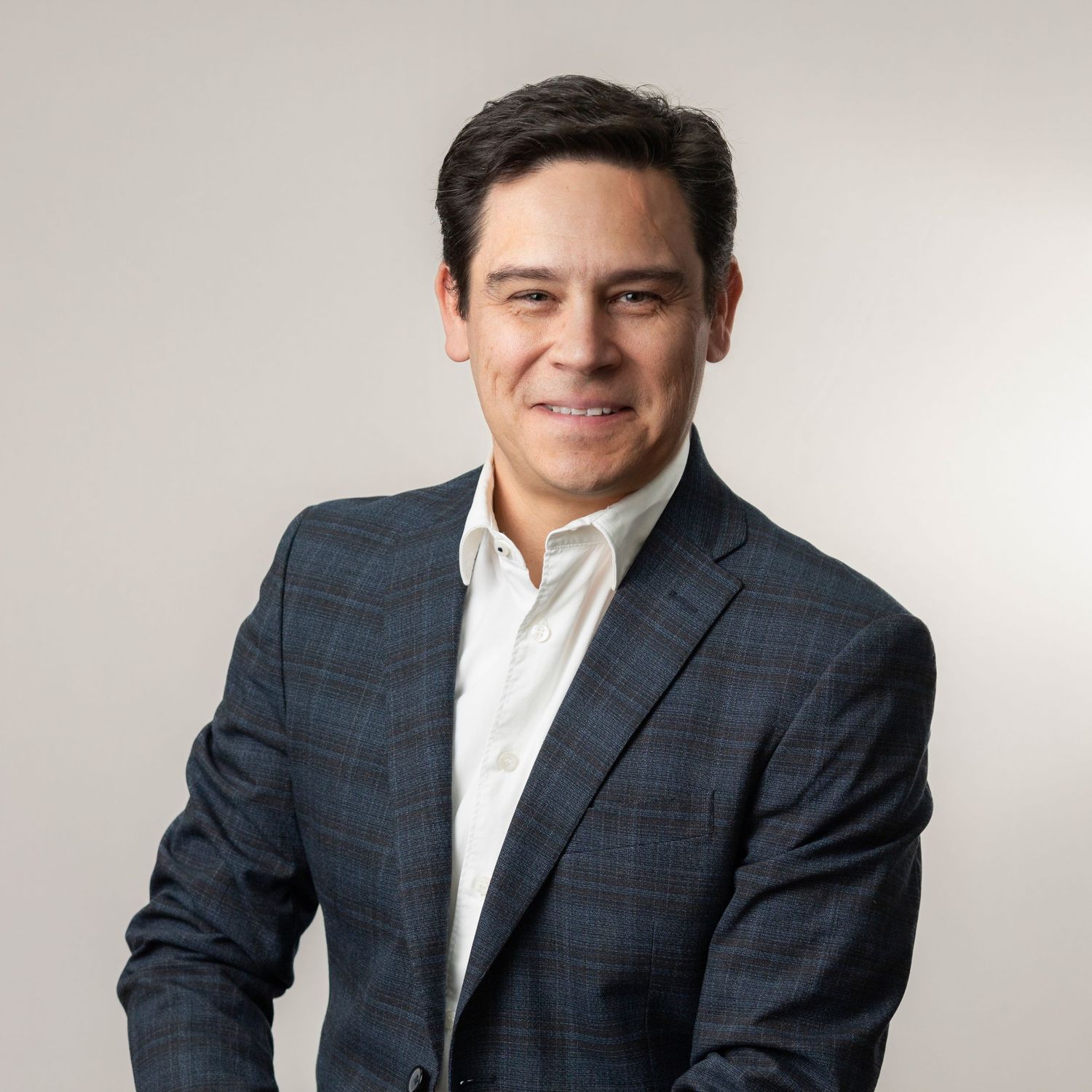 Professional headshot of someone wearing a navy checkered suit jacket and white dress shirt against light background.